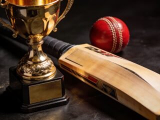 Golden cricket trophy beside a bat and red leather ball in dramatic studio lighting